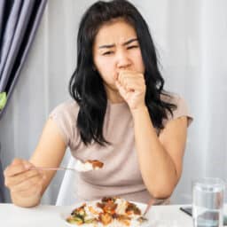 Woman coughing on a bite of food.