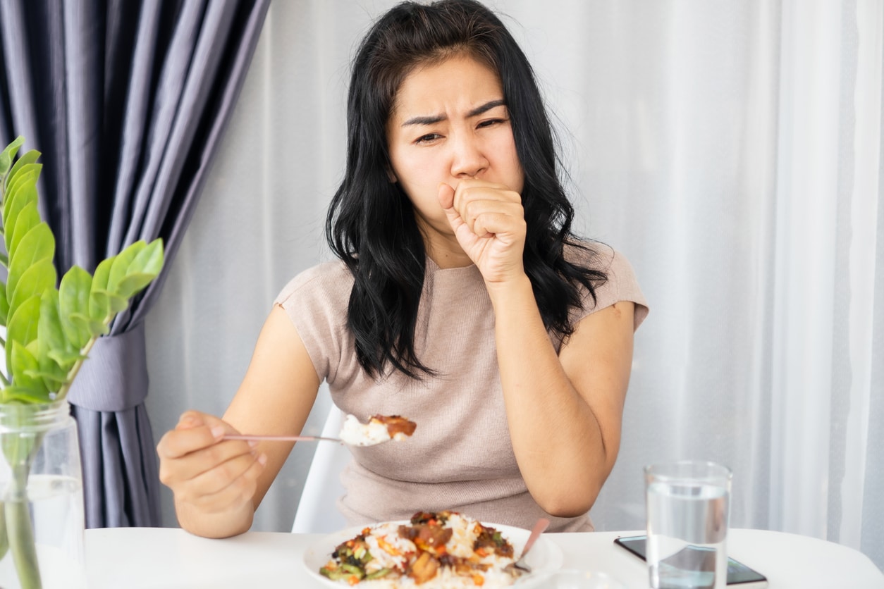 Woman coughing on a bite of food.