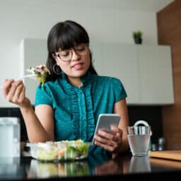 Woman eating her lunch while looking at her phone.