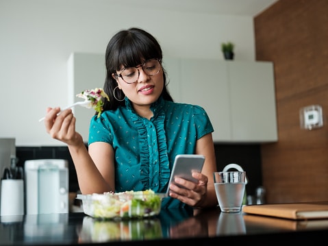 Woman eating her lunch while looking at her phone.