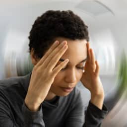 Dizzy woman holding her head, blurred background.