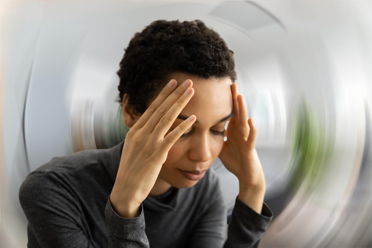 Dizzy woman holding her head, blurred background.