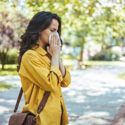 Close-up of a young woman blowing nose with tissue paper at the park.