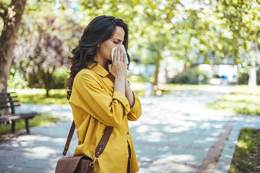 Close-up of a young woman blowing nose with tissue paper at the park.
