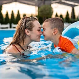 Young boy swimming with his mom in the pool.