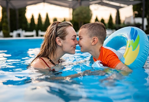 Young boy swimming with his mom in the pool.