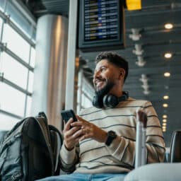 A man holding his smartphone and smiling while waiting to board at the airport.